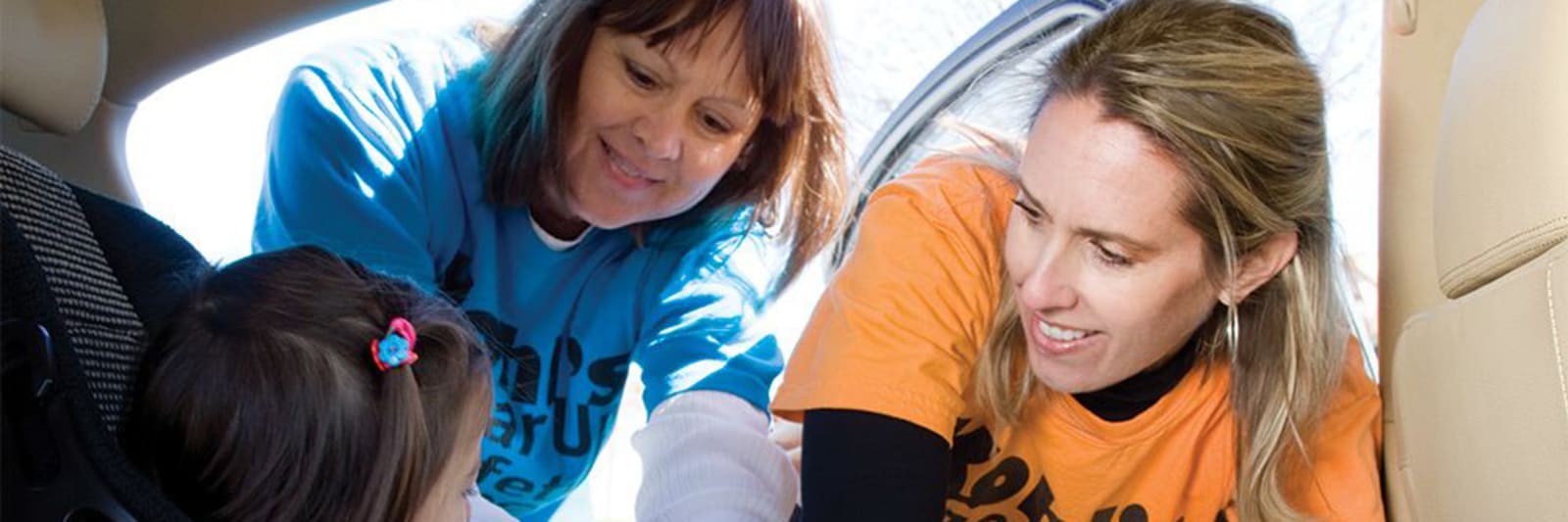 two women strapping a child into a carseat in the back of a car