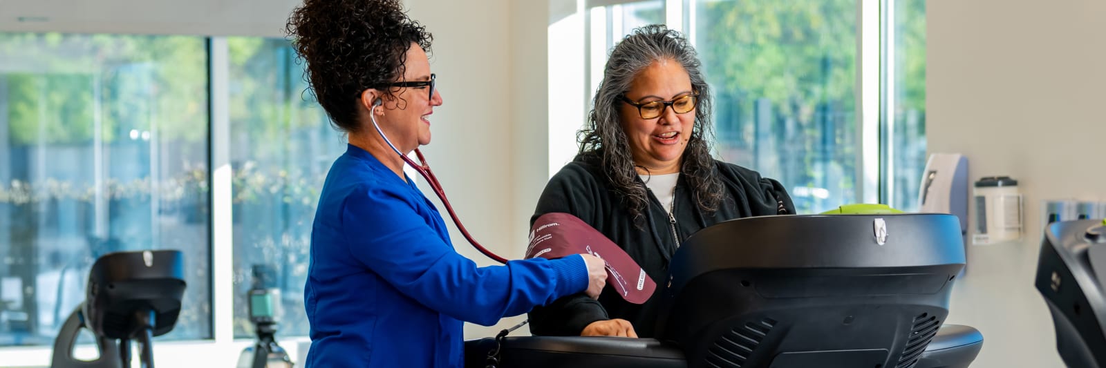 woman walks on a treadmill while a nurse looks on