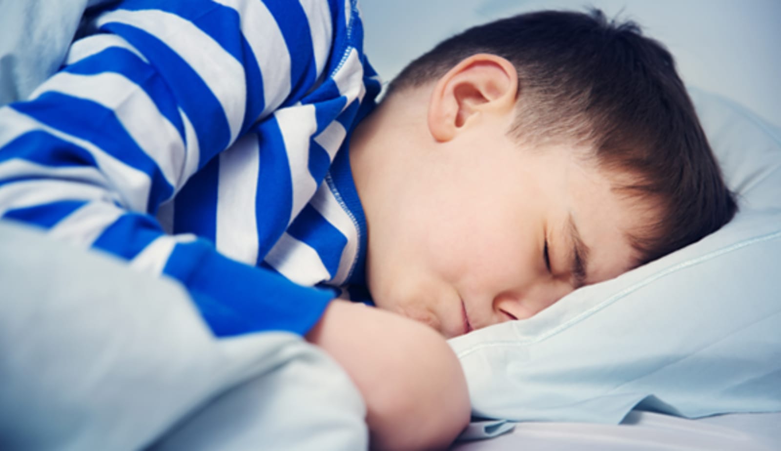 young boy laying in bed sleeping with a pained expression on his face