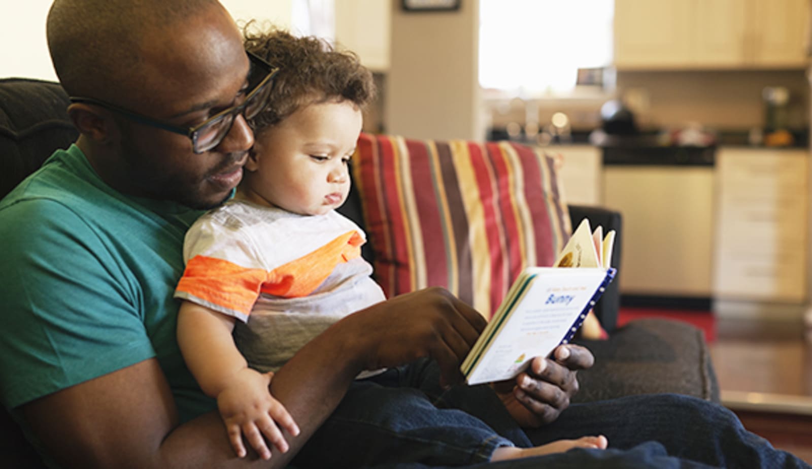 A father is reading a book to a toddler on a couch