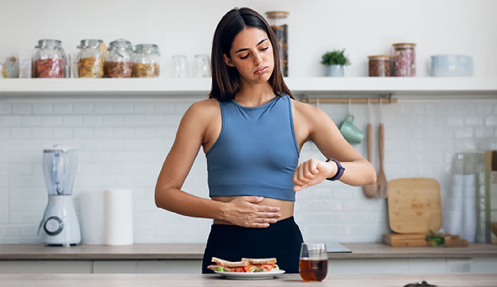 A woman looking at her watch and hold her stomach like she's hungry