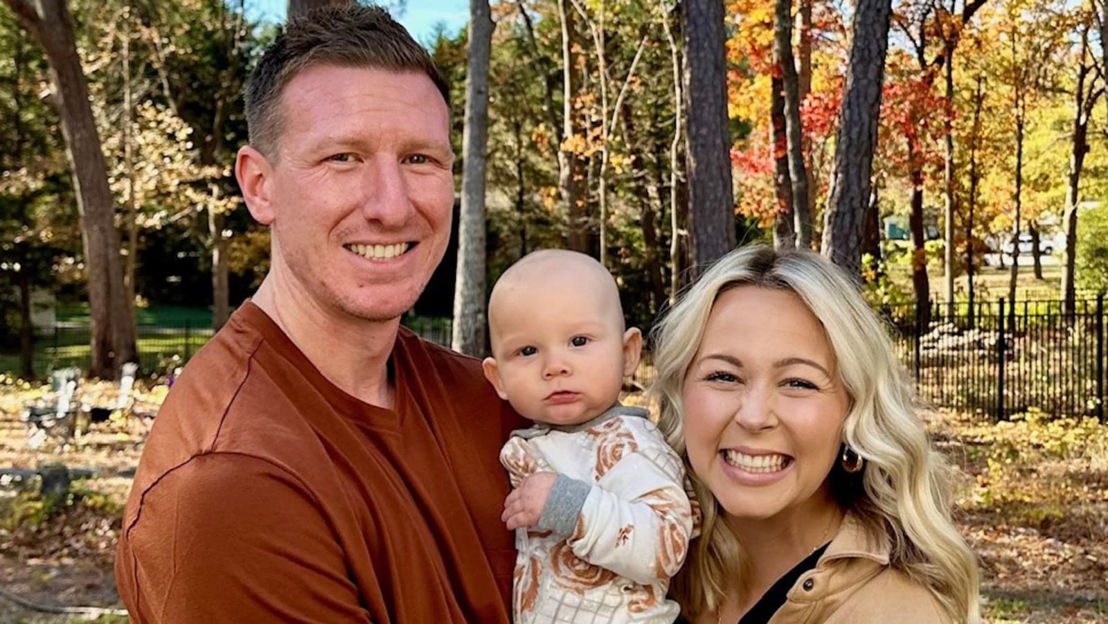 smiling couple holding a baby outside during fall