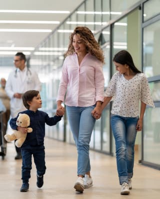 smiling mother holding the hands of her 2 children while walking at the hospital, with a doctor in the background