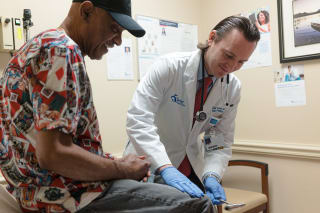 smiling male doctor testing the reflexes of a smiling male patient
