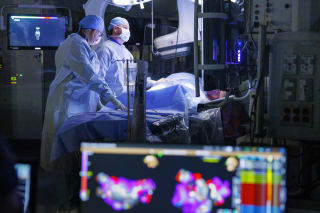 two baptist health heart surgeons performing a procedure in a dark operating room with lighting focused on patient, along with a colorful computer screen in the foreground.