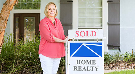 woman standing next to sold realty sign