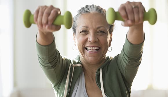 older Hispanic woman lifting weights in living room