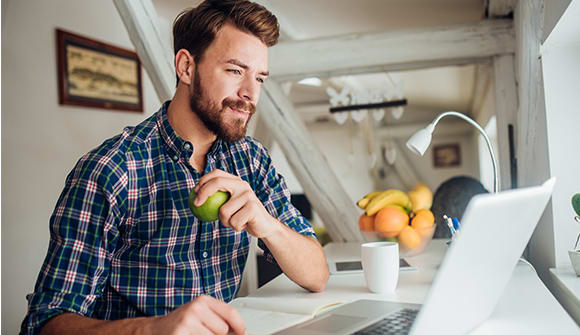 man eating apple at his laptop