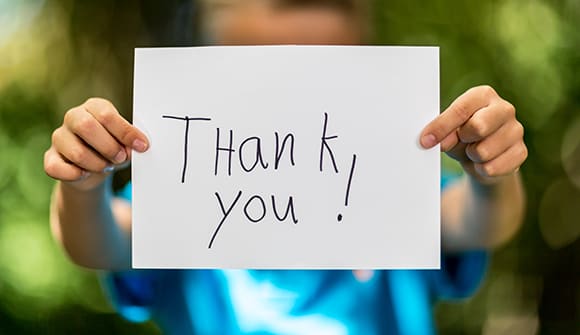 a child holding up a hand written sign that says thank you