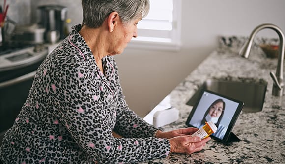 senior aged woman in her kitchen, using a tablet for a virtual appointment with a doctor