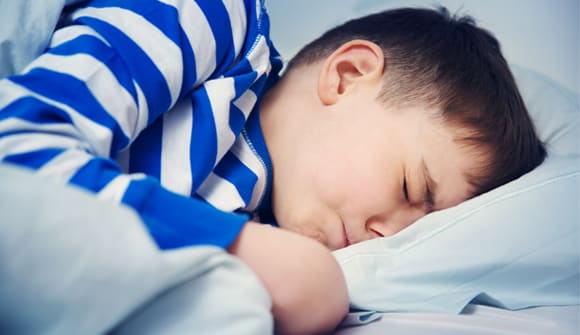 young boy laying in bed sleeping with a pained expression on his face