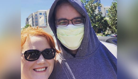 close up of a man in a mask and hoodie standing next to a woman in sunglasses