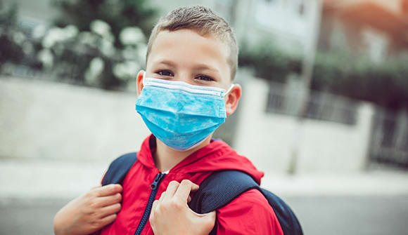 close up of smiling young boy wearing a disposable mask and backpack
