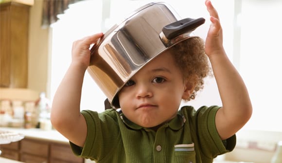 small boy in a green shirt with a large pot on his head