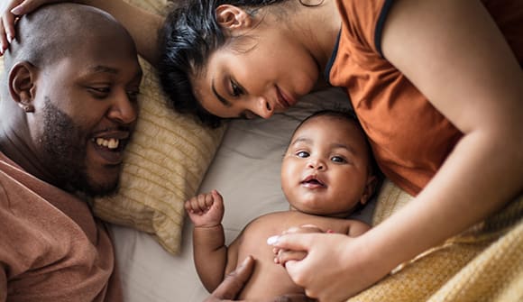 mother, father and young baby laying down in a bed together