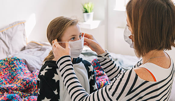 mother wearing a disposable mask putting a different mask on her daughter
