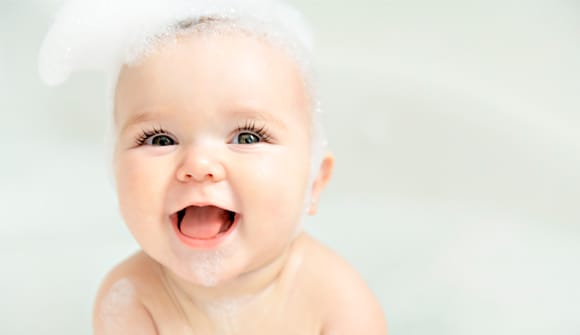 smiling baby in a bathtub with bubbles on her head and shoulders