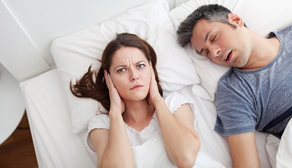 woman with hands over her ears with husband sleeping