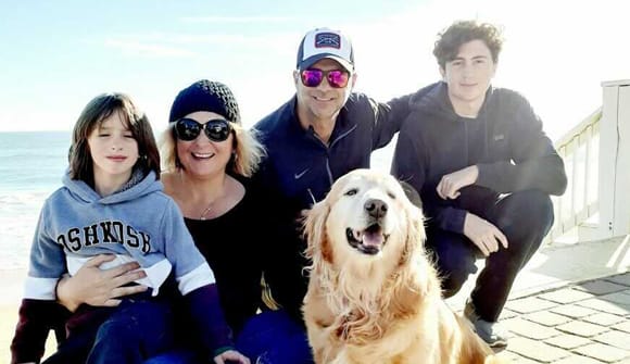 Smiling family sits on a porch with their dog in front of the ocean