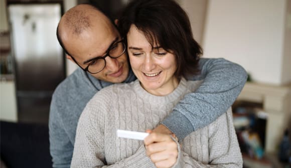 man and woman looking at a pregnancy test while embracing