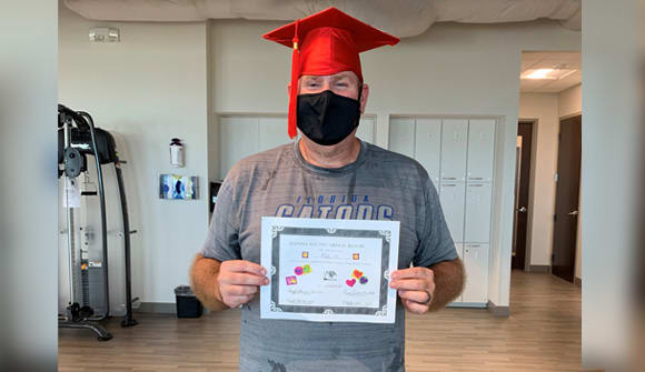 man wearing a graduation cap and mask while holding a diploma