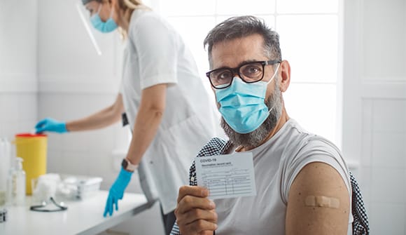 masked man holding his covid-19 vaccine card