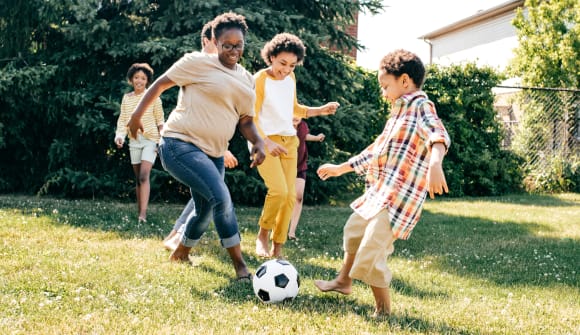 Woman kicking the soccer ball with children outside on a sunny day. 