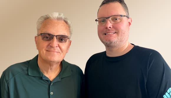 father and son standing next to each other in front of a blank wall