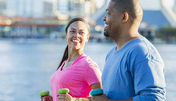 smiling couple walking with free weights by the river