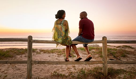 Smiling couple sitting on a fence overlooking the beach