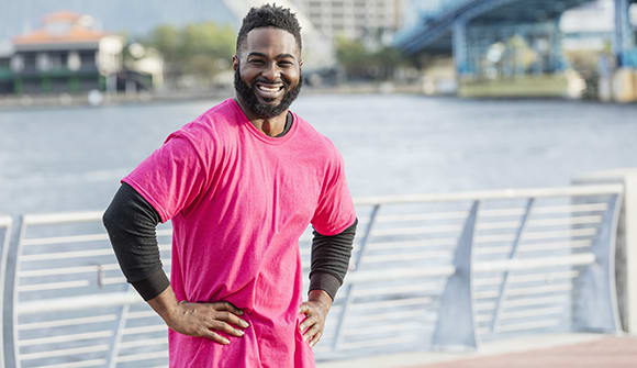 Man wearing a pink shirt stands in front of the river.