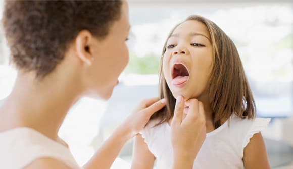 A little girl opens her mouth and sticks out her tongue to show her mother the inside of her throat. 