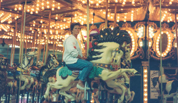 A woman sitting on a horse on a merry-go-round staring out into the distance.