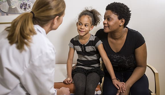 mom and elementary-aged daughter meet with female pediatrician for her annual checkup