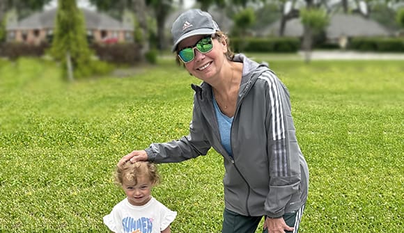 Smiling grandmother in gray jacket, gray hat and gray sunglasses with her hand on her smiling granddaughter's head.
