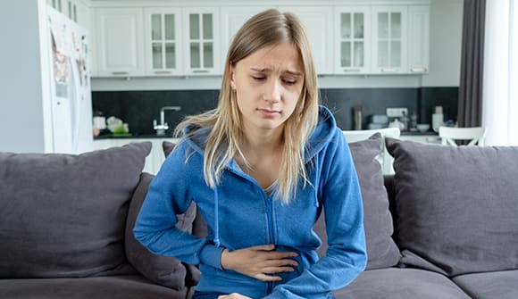 teenage girl holds her hand on a sore stomach while sitting on a couch