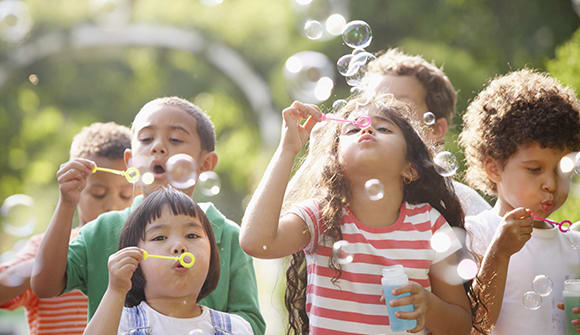 Several children blowing bubbles outside during summer break.
