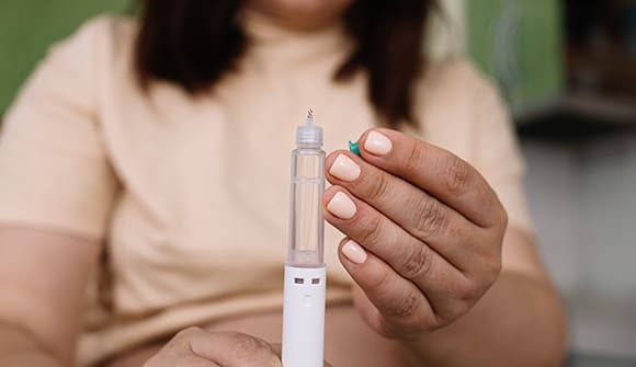 Weight Loss Drugs vs. Surgery: What's a better long-term solution?  Woman holding an injectable shot of weight loss drugs.