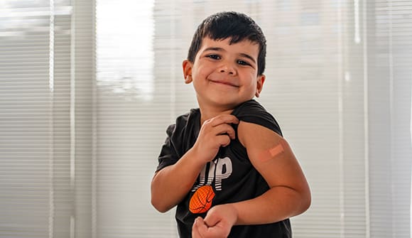 Little boy shows off bandage on upper arm regarding a shot