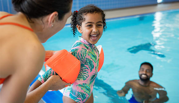 Child with flotation devices on arms smiling with parents in a pool
