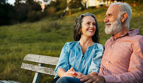 A senior couple happy and sitting on a park bench together