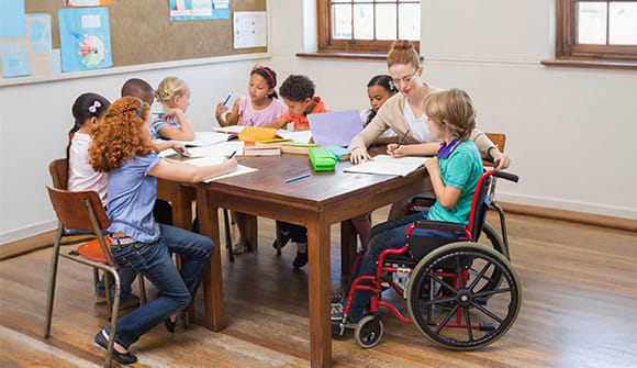 Children sitting at a table with an adult and one child is in a wheelchair