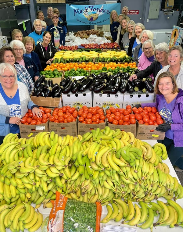a large group of volunteers at pie in the sky surrounded by boxes and crates of fresh fruits and vegetables.