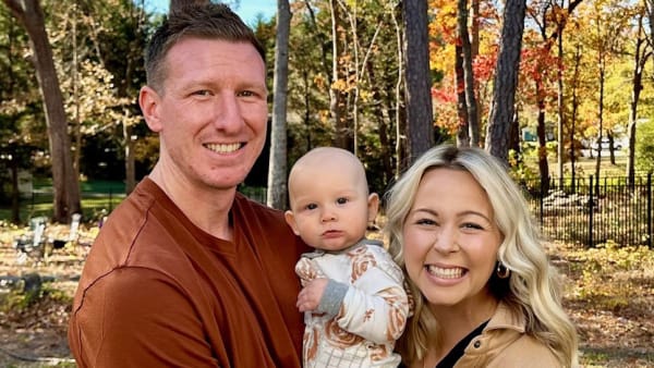 smiling couple holding a baby outside during fall