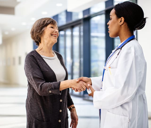 A female physician shakes hands with a female, senior patient wearing a cardigan.