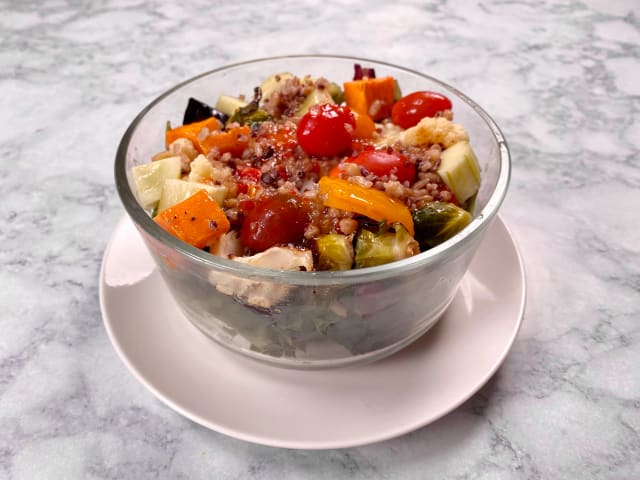 brightly colored vegetables and quinoa in a clear bowl sitting a marble counter top