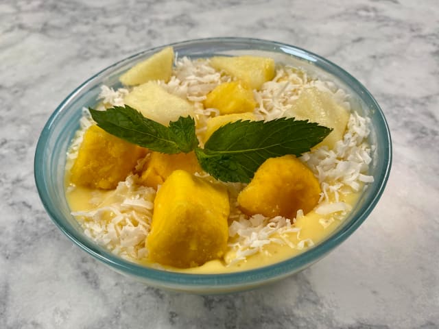 mango and pineapple smoothie bowl topped with coconut flakes and mint
