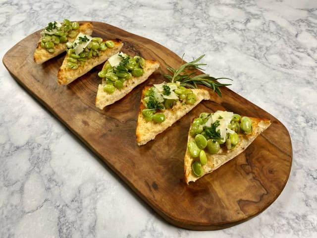 small bruschetta triangles with broad beans and pecorino cheese sitting on a wooden serving board on top of a marble countertop