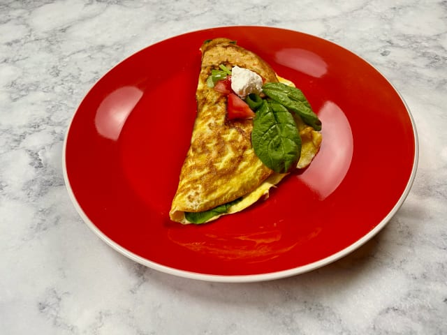 Spinach and goat cheese omelette on a red plate sitting on a marble counter top