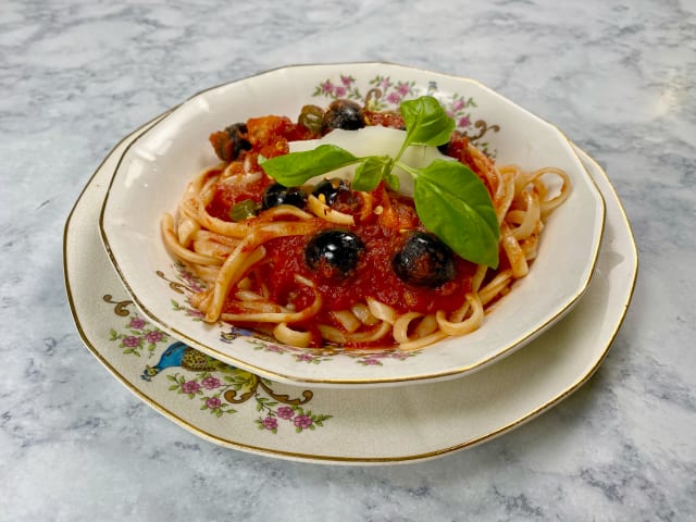pasta with red sauce, olives, cheese and basil in a fancy gold rimmed bowl sitting on a marble counter